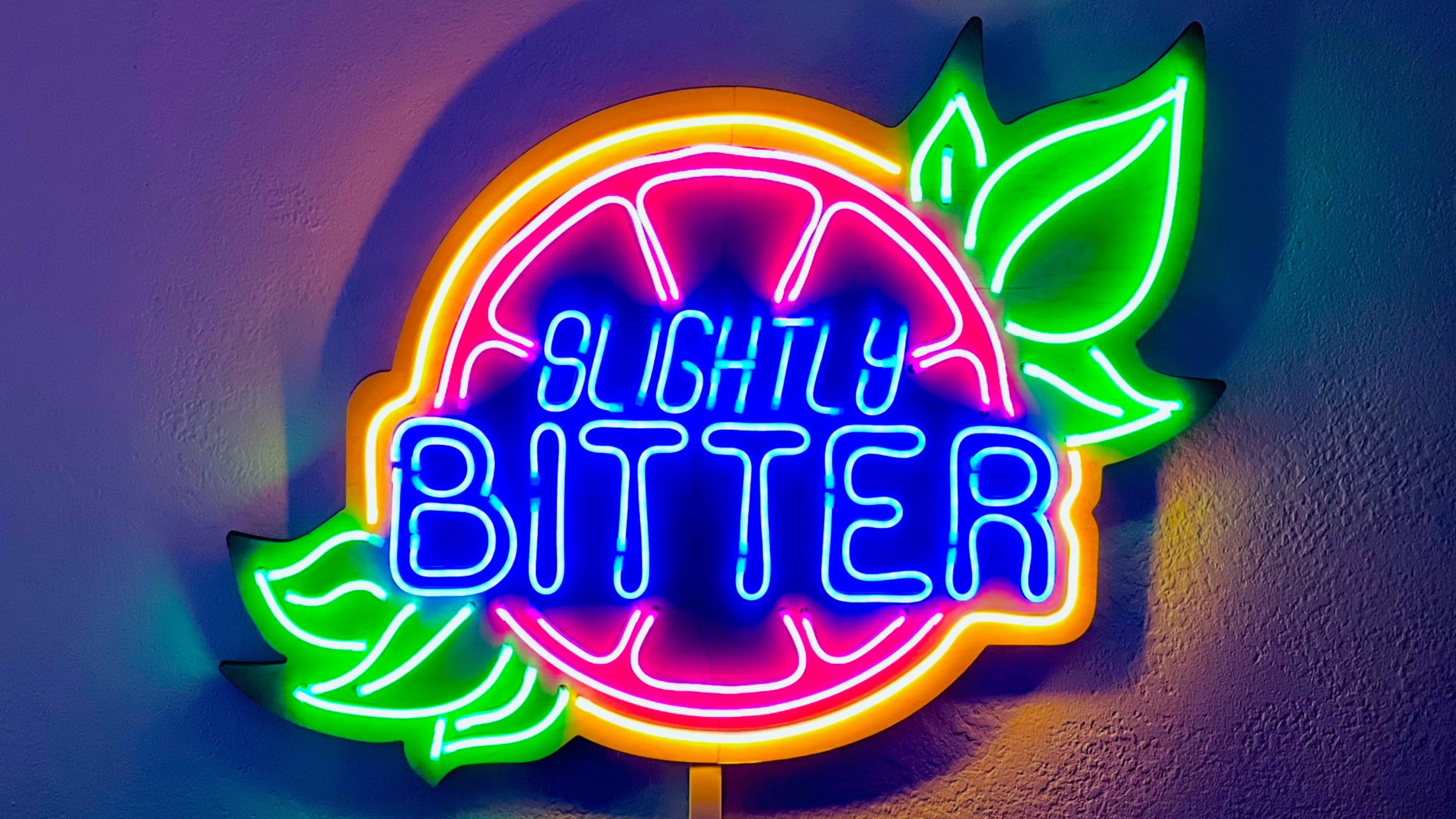 A neon sign in the shape of a grapefruit that says 'Slightly Bitter'.
